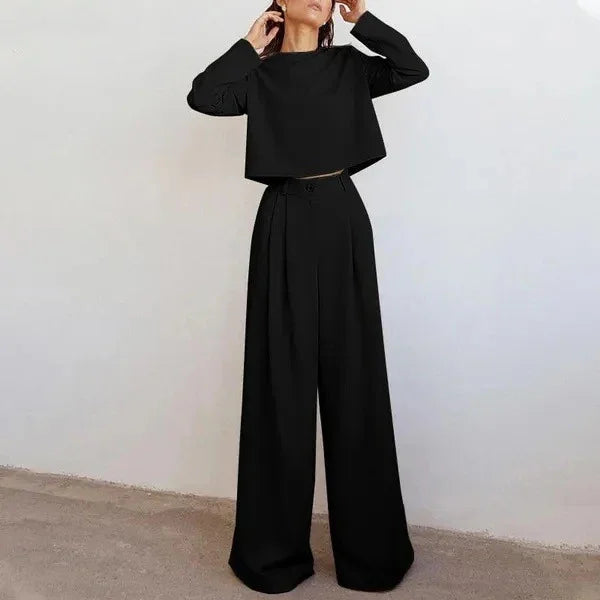 Woman wearing a minimalist black long-sleeve crop top and wide-leg high-waist pants against white wall