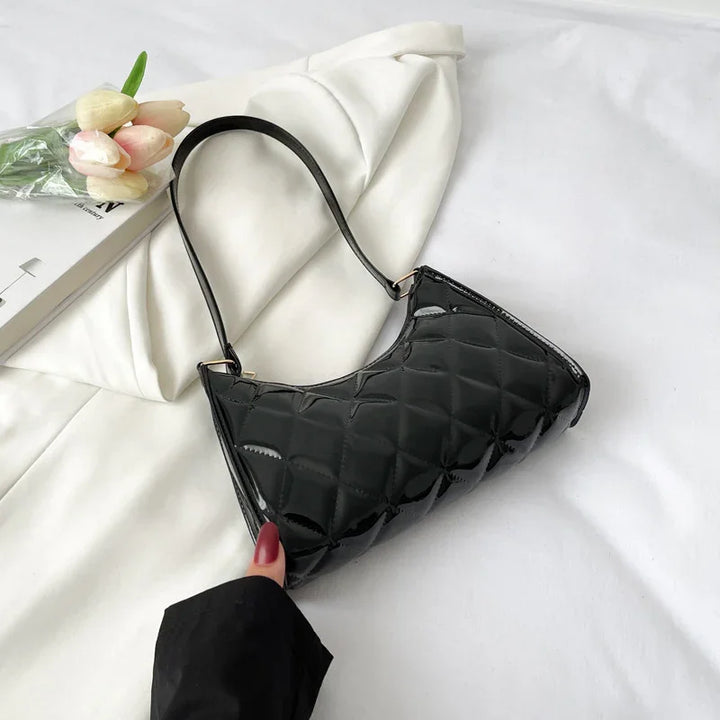 Black quilted patent leather handbag with shoulder strap on white fabric, tulips and magazine nearby