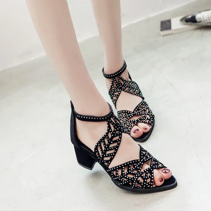 Black open-toe block heel sandals with studded geometric straps on model's feet