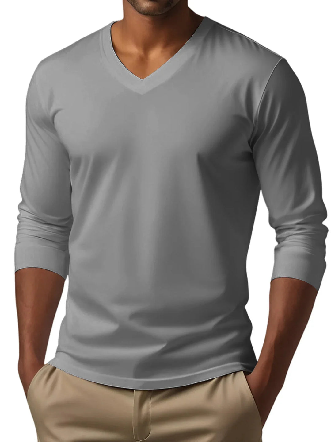 Man wearing a fitted grey V-neck long sleeve shirt tucked into beige pants with hands in pockets