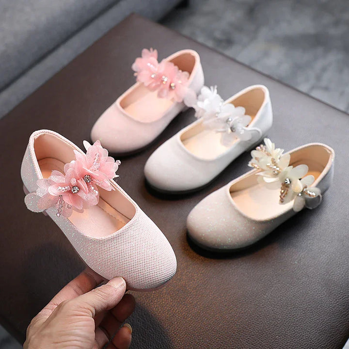 Three pairs of elegant baby girl shoes with flower and pearl decorations in pink, white, and cream colors