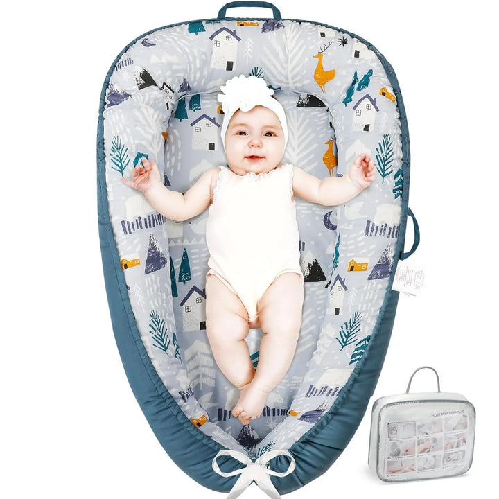 Baby in white outfit lying in a blue and gray padded baby nest with animal and house prints