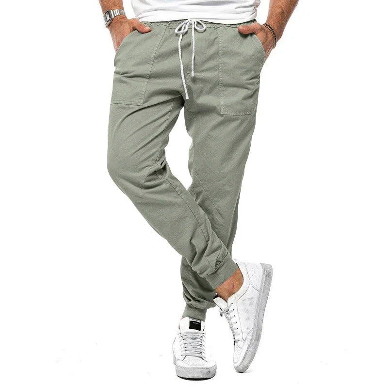 Man wearing light green casual jogger pants with pockets and white sneakers on white background