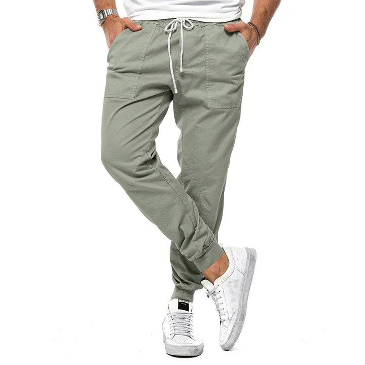 Man wearing light green casual jogger pants with pockets and white sneakers on white background