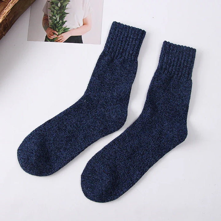 Pair of dark blue knitted wool winter socks on a white background with a photo of a person holding green leaves