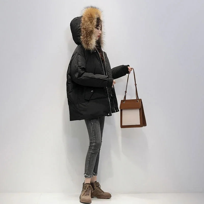 Woman wearing black puffer jacket with fur hood, gray skinny jeans, brown boots, holding brown handbag