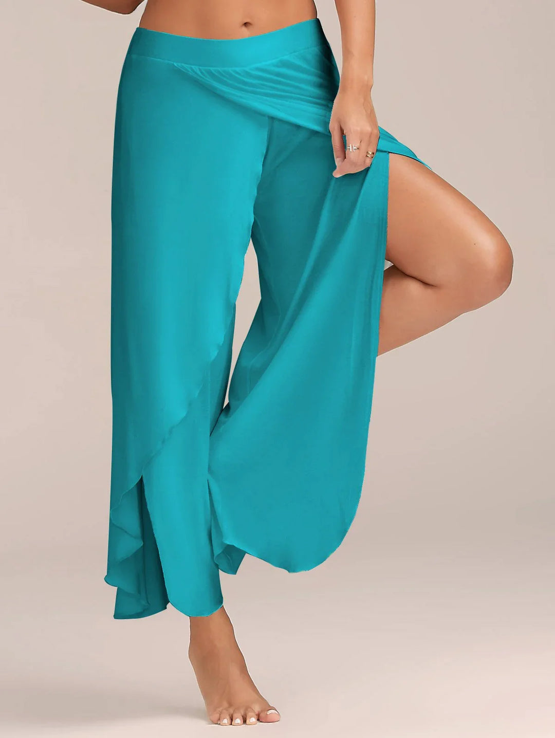 Woman wearing turquoise wide-leg pants with high slit detail, barefoot on neutral background