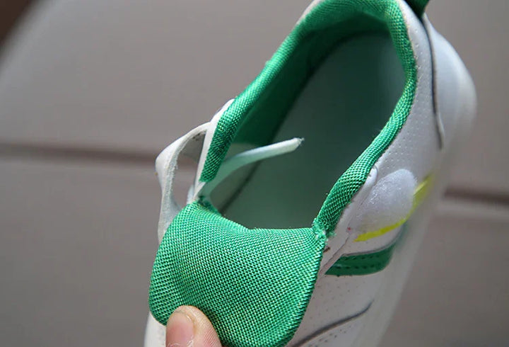 Close-up of white sneaker with green inner lining and tongue held by hand on tiled floor