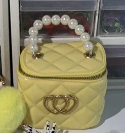 Yellow quilted handbag with pearl handle and gold double-ring clasp on white surface