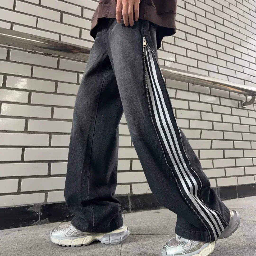 Person wearing black wide-leg pants with side zippers and white stripes, standing by tiled wall.