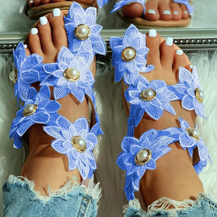 Close-up of feet wearing blue floral sandals with pearl centers and white toenail polish