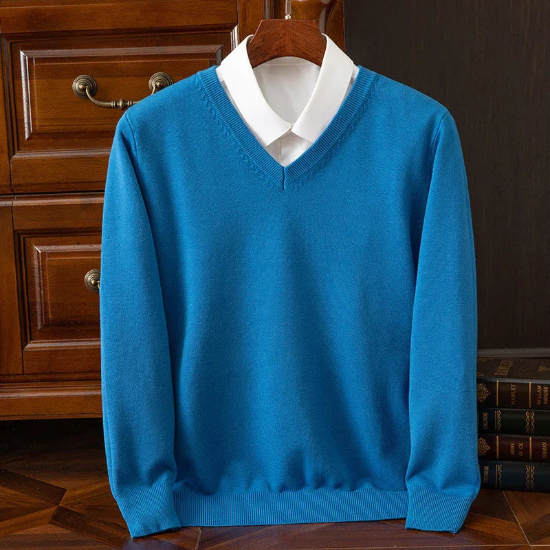 Blue V-neck sweater over white collared shirt displayed on wooden hanger with wooden dresser and books background
