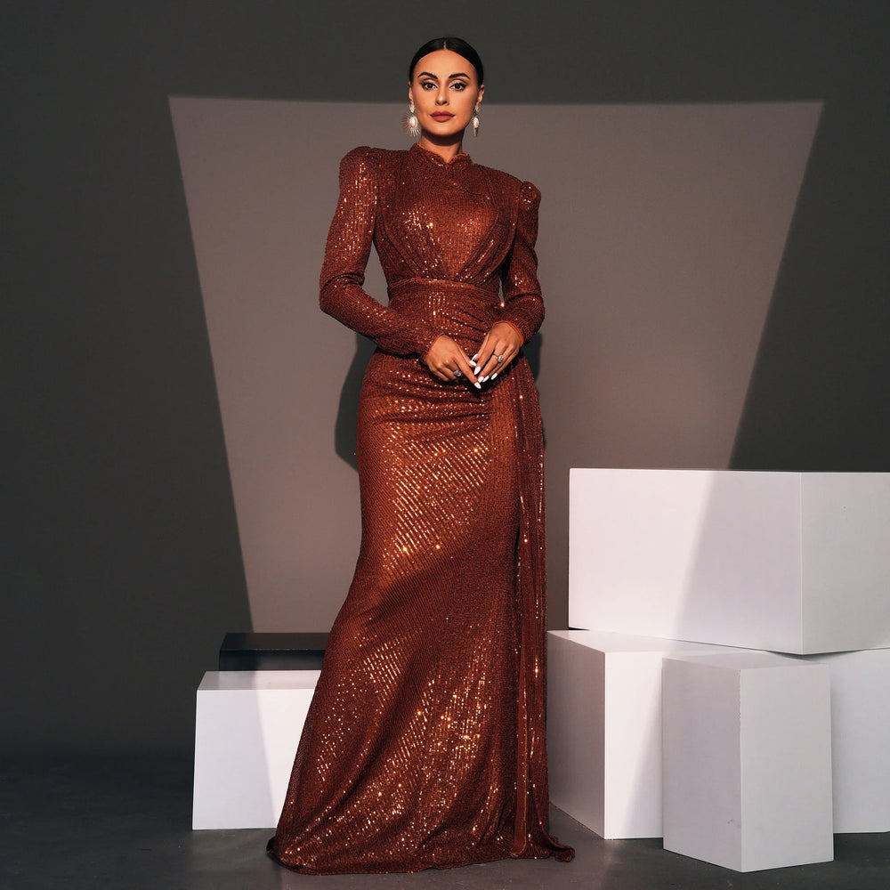 Woman in elegant long-sleeve sequin brown gown with dramatic shoulder pads, posing indoors