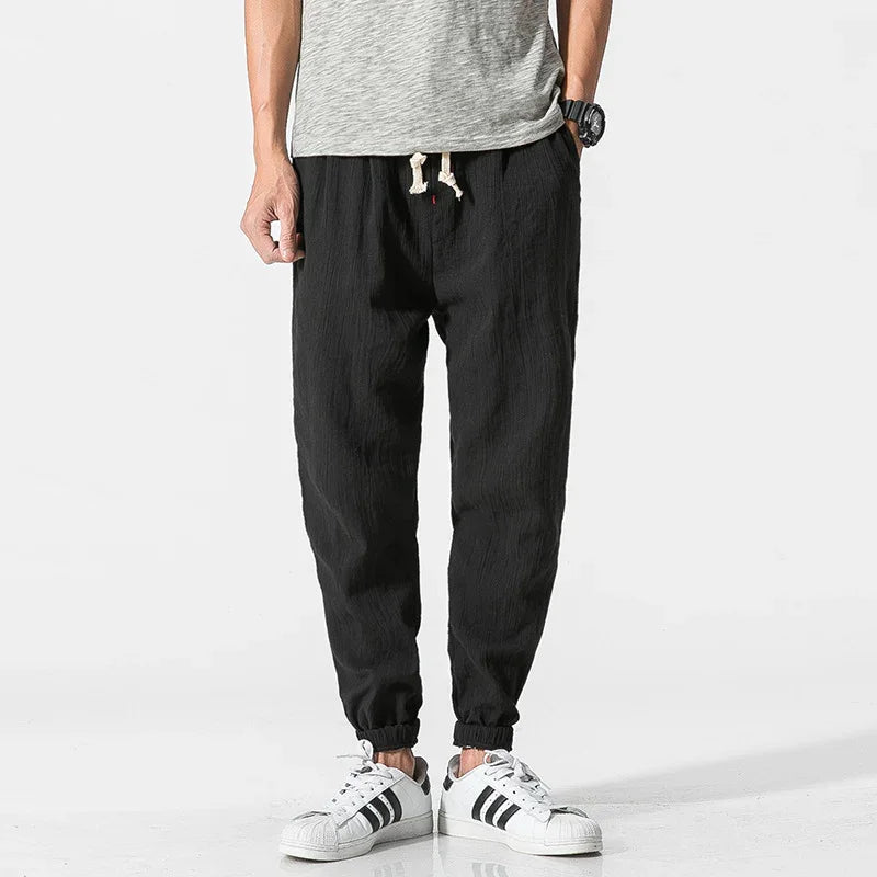 Man wearing black drawstring jogger pants with elastic cuffs and white sneakers with black stripes