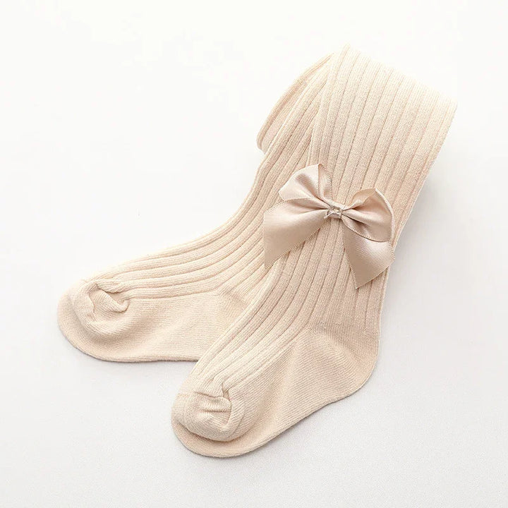 Cream-colored ribbed baby tights with a satin bow detail on a white background