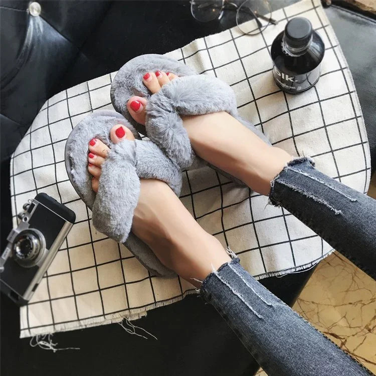 Feet wearing soft gray fuzzy slippers with crossed straps on checkered fabric and torn skinny jeans