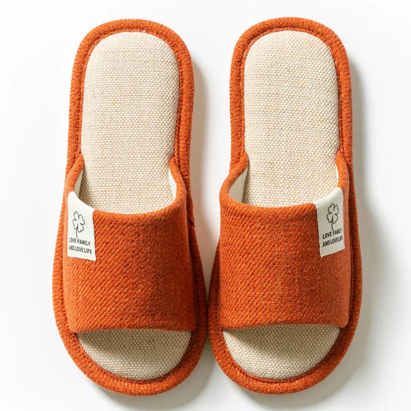 Pair of orange and beige indoor slippers with fabric label on white background