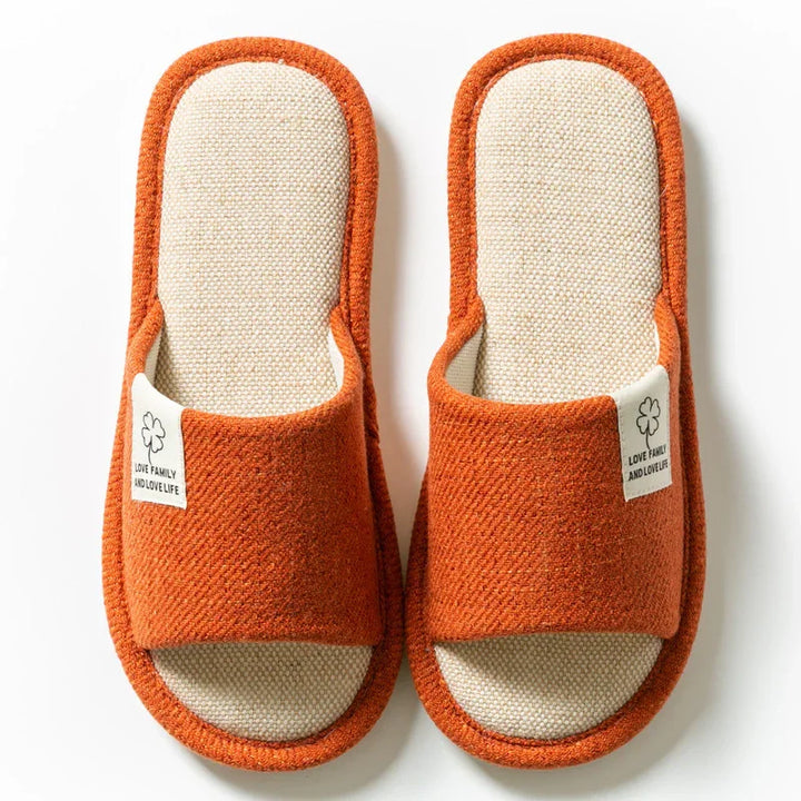 Pair of orange and beige indoor slippers with fabric label on white background