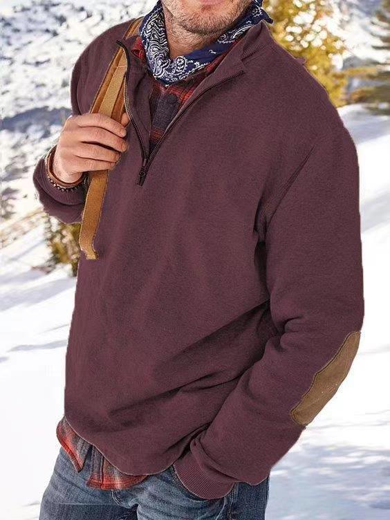 Man wearing a maroon quarter-zip fleece pullover with elbow patches, plaid shirt, and carrying a leather strap bag in a snowy outdoor setting