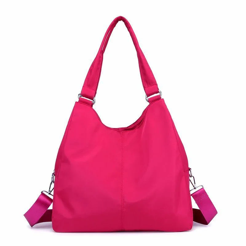 Bright pink nylon shoulder bag with dual handles and detachable strap on white background