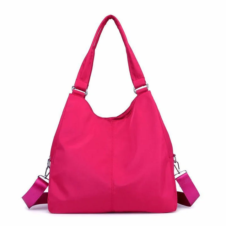 Bright pink nylon shoulder bag with dual handles and detachable strap on white background