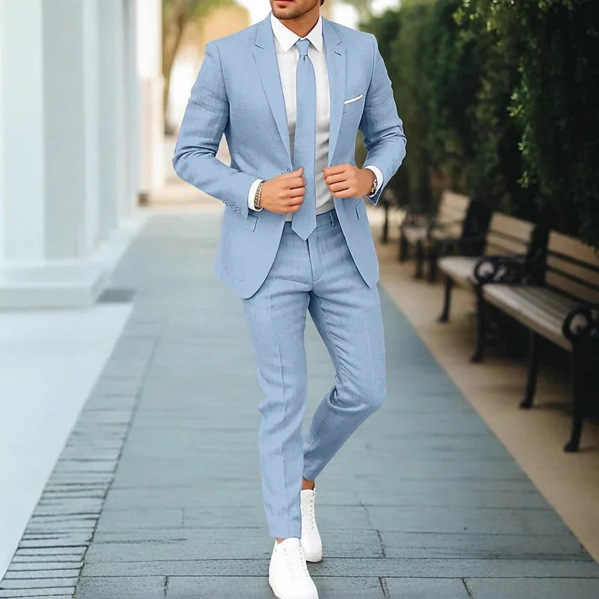 Man wearing a light blue slim fit suit with white dress shirt and tie, paired with white sneakers on a paved walkway