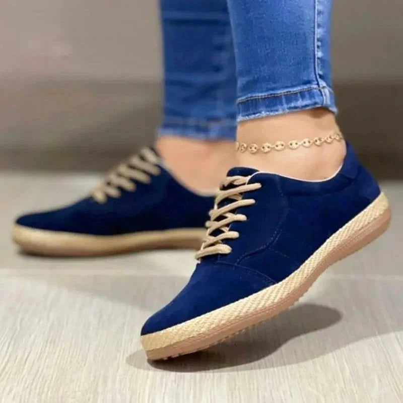 Women wearing navy blue casual sneakers with beige laces and woven sole, paired with blue jeans and gold anklet