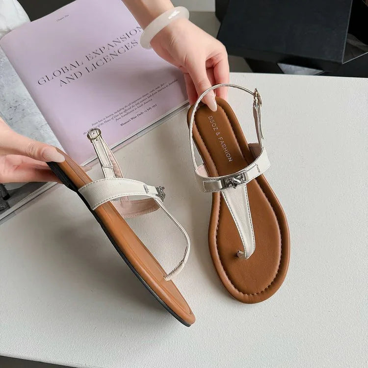 White leather thong sandals with cushioned brown insoles and adjustable ankle straps on white table