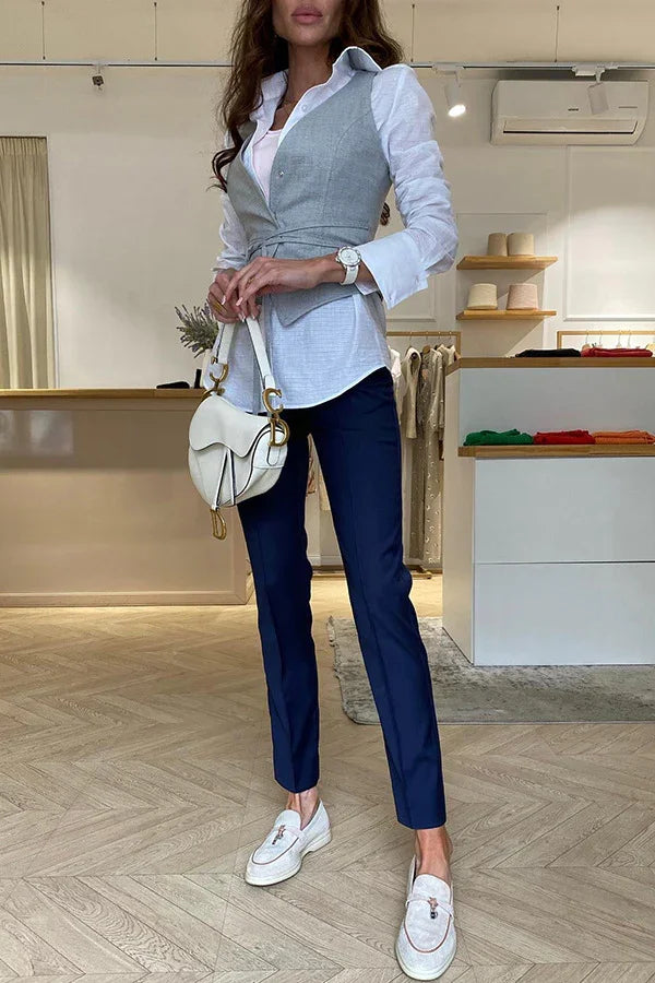Woman in modern boutique wearing light gray vest, white shirt, navy pants, white loafers, holding white designer handbag