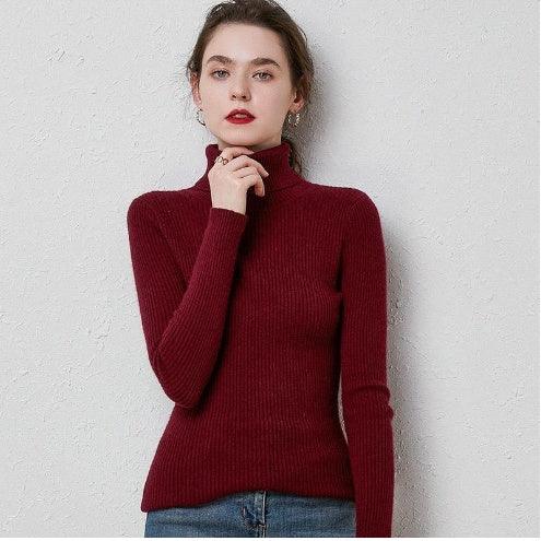 Woman wearing a ribbed burgundy turtleneck sweater and blue jeans against a gray textured wall