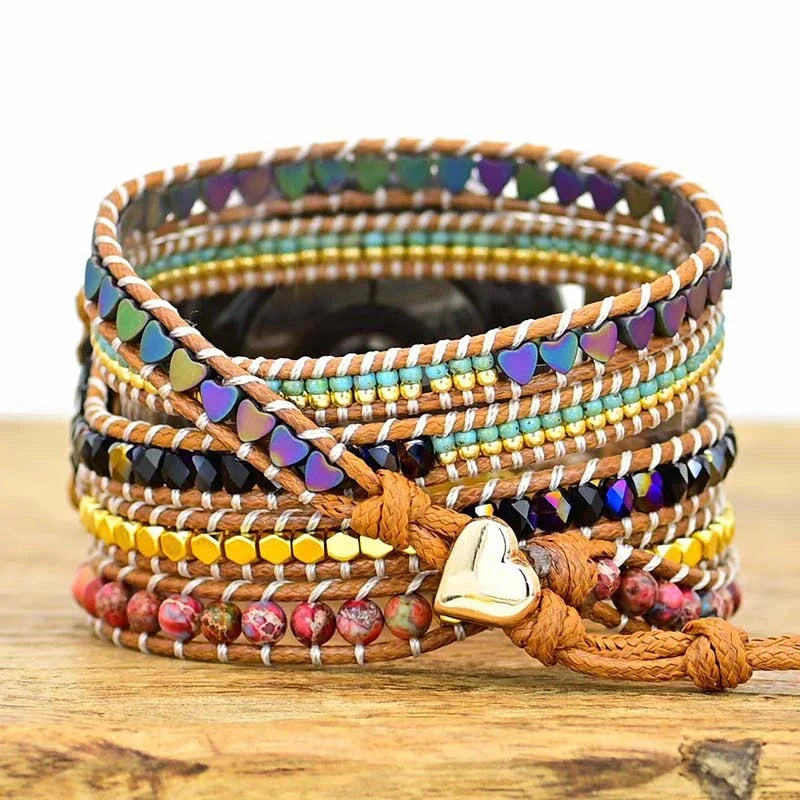 Colorful beaded wrap bracelet with heart-shaped charm on brown cord, displayed on wooden surface