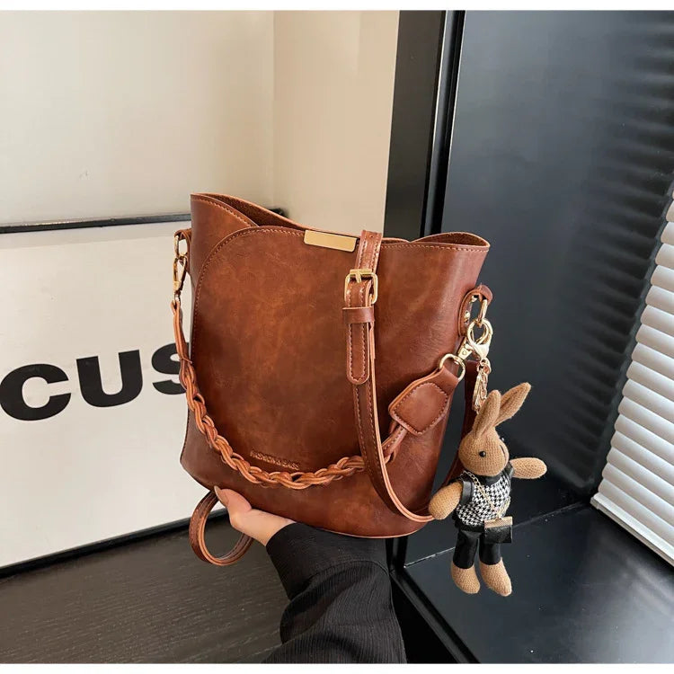 Brown leather bucket bag with braided strap and cute bunny keychain in modern indoor setting