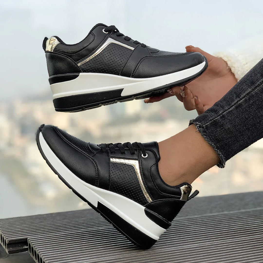 Black leather sneakers with white soles and gold accents worn outdoors with cityscape background