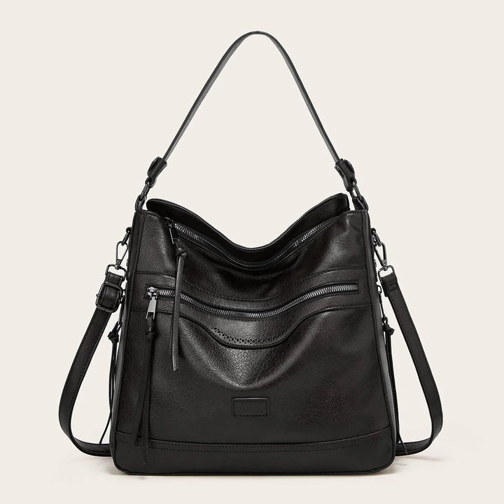 Black leather shoulder bag with front zipper pocket and adjustable strap on beige background