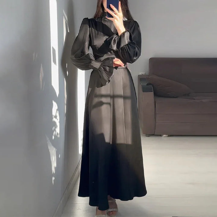 Woman wearing a long black satin dress with puffed sleeves and ruffled cuffs in a bright room