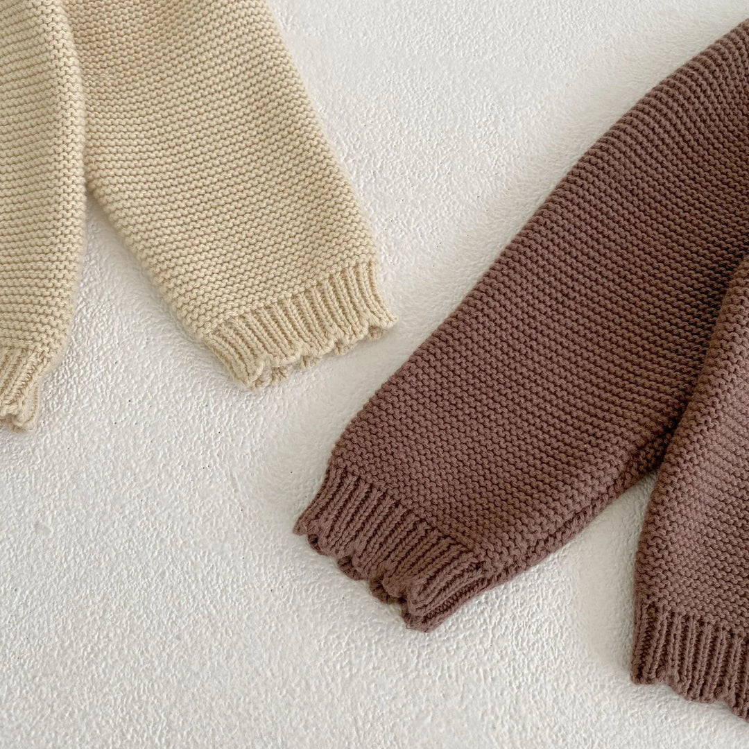 Close-up of cream and brown knitted sweater sleeves with textured pattern on white surface