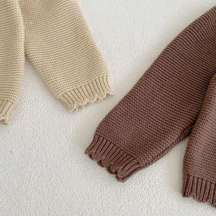 Close-up of cream and brown knitted sweater sleeves with textured pattern on white surface