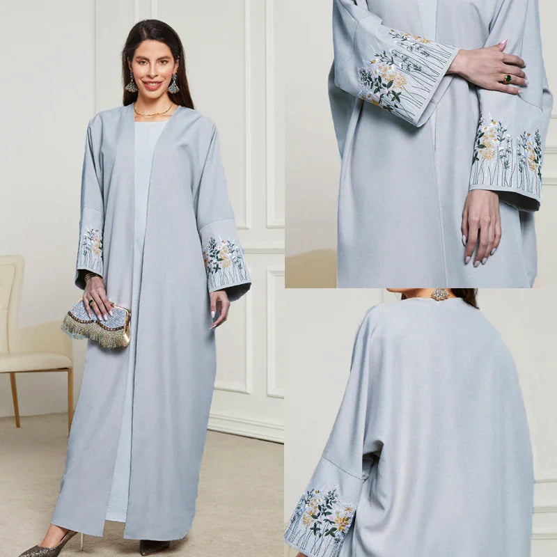 Woman wearing light blue long abaya with floral embroidery on wide sleeves, holding beaded clutch