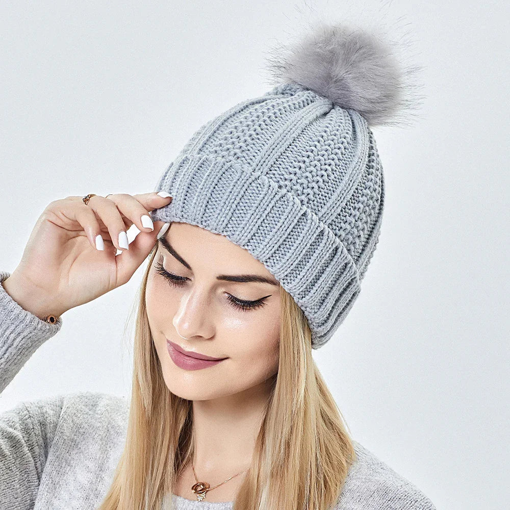 Woman wearing light gray knit winter beanie hat with fluffy pom-pom, matching sweater, white nails