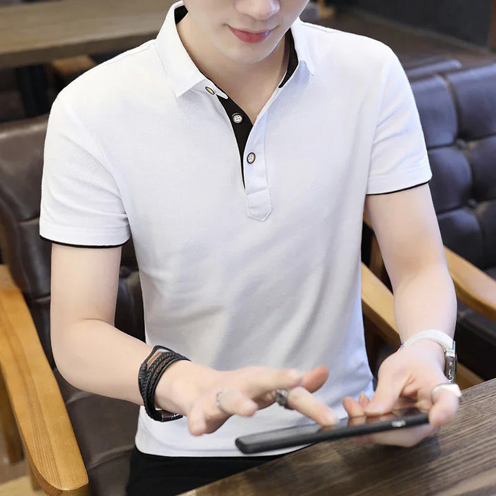 Man wearing white polo shirt with black trim using smartphone indoors on wooden table