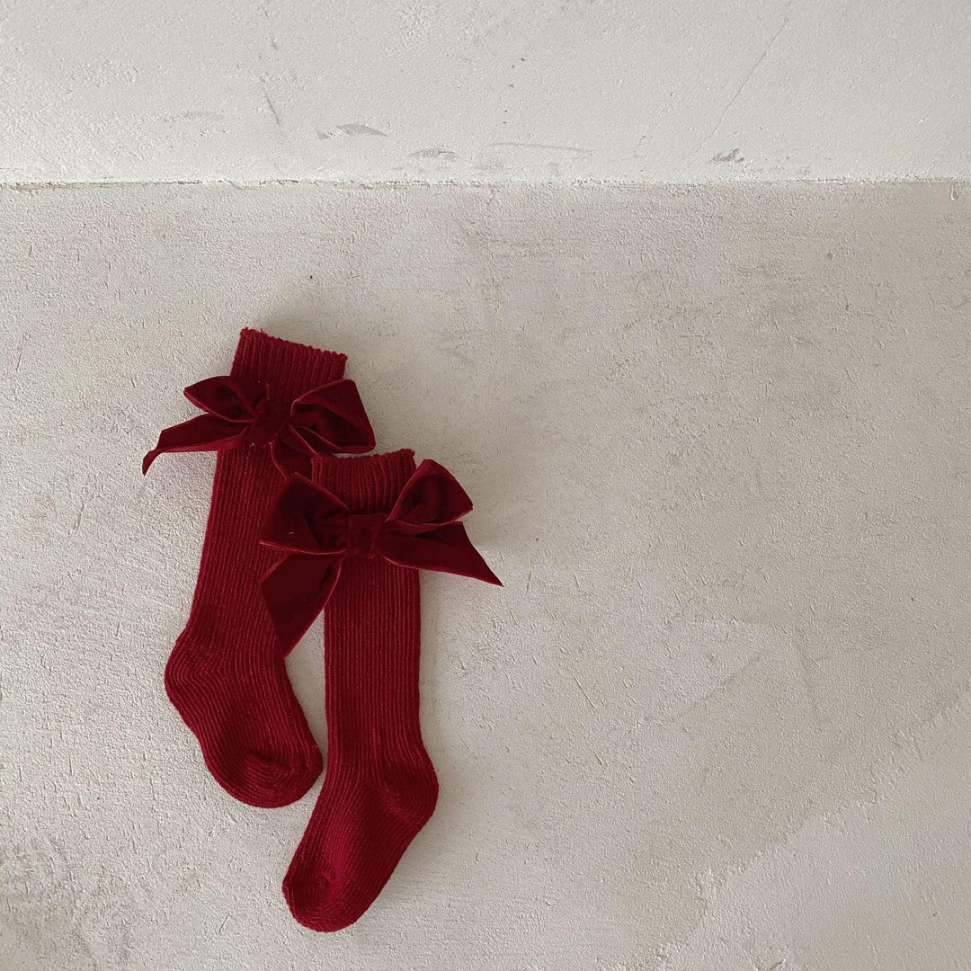 Pair of red knit knee-high socks with large velvet bows on textured beige floor