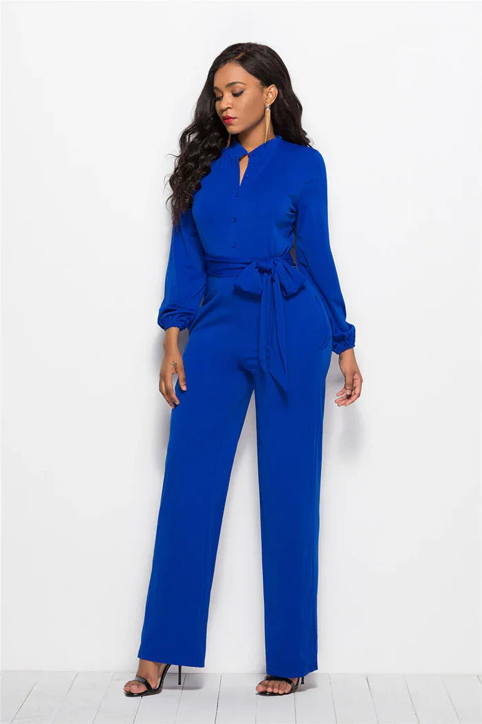 Woman in royal blue long-sleeve jumpsuit with waist tie and black high heel sandals