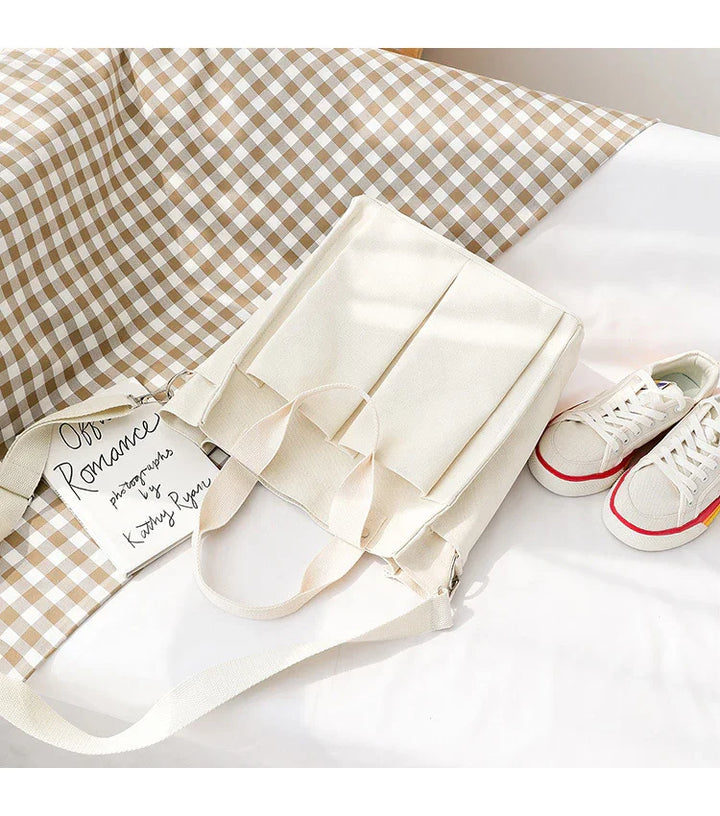 Cream canvas tote bag with front pockets, beige gingham fabric, and white canvas sneakers with red and yellow stripes