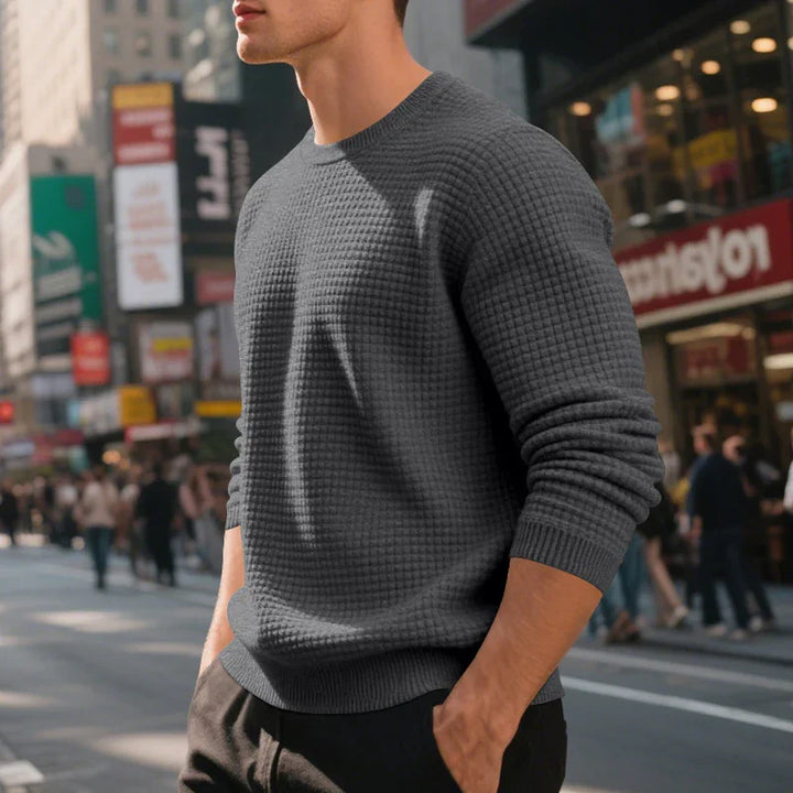 Man wearing a textured dark gray sweater standing in urban city street with blurred crowds