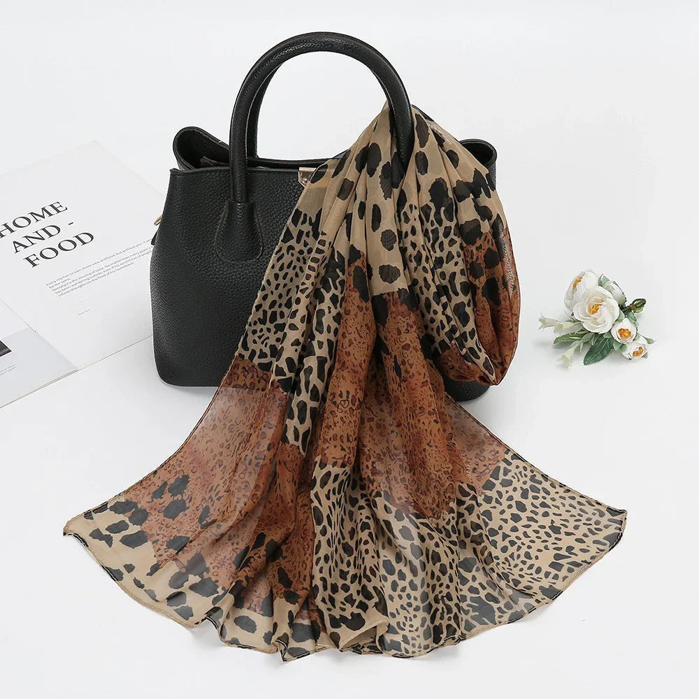 Black leather handbag with light brown and dark brown leopard print scarf draped over handle on white surface