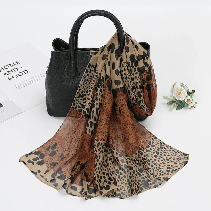 Black leather handbag with light brown and dark brown leopard print scarf draped over handle on white surface