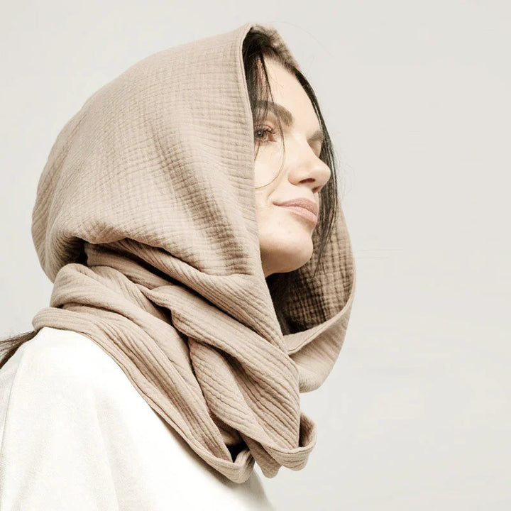 Woman wearing a beige textured hooded scarf with a neutral background