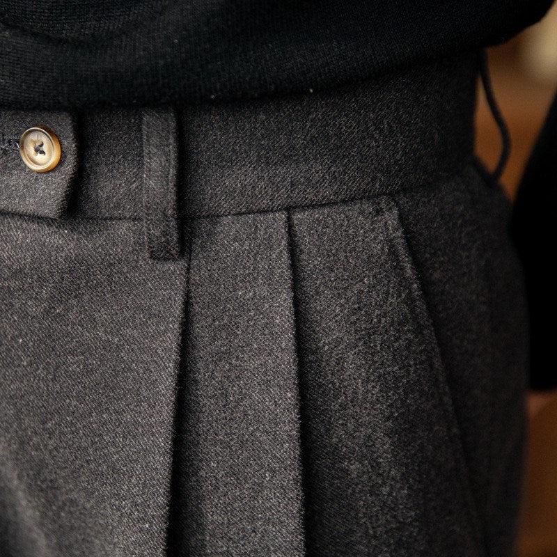 Close-up of dark gray wool trousers with front pleats and a brown button detail