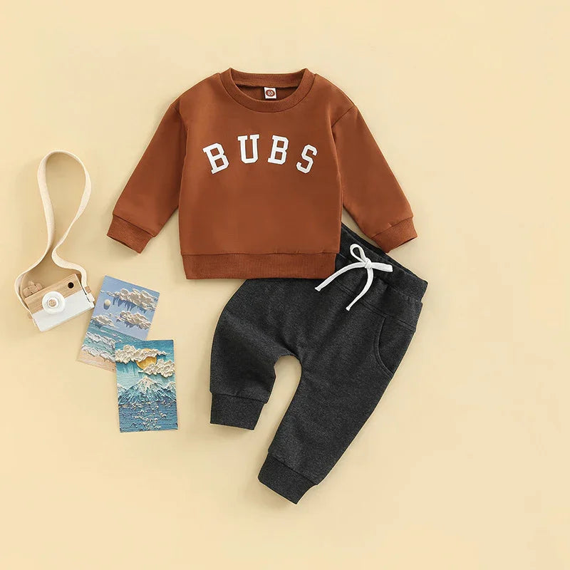 Toddler outfit with brown sweatshirt reading BUBS and dark gray jogger pants on beige background