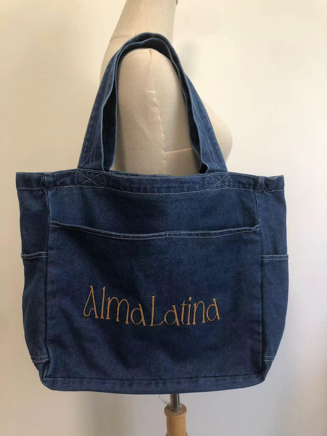 Dark blue denim tote bag with front pocket and AlmaLatina embroidered in gold